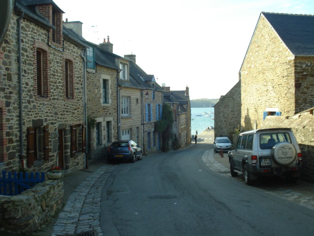 Rue en pente bordée de maisons en granit à Saint-Suliac, descendant vers la Rance